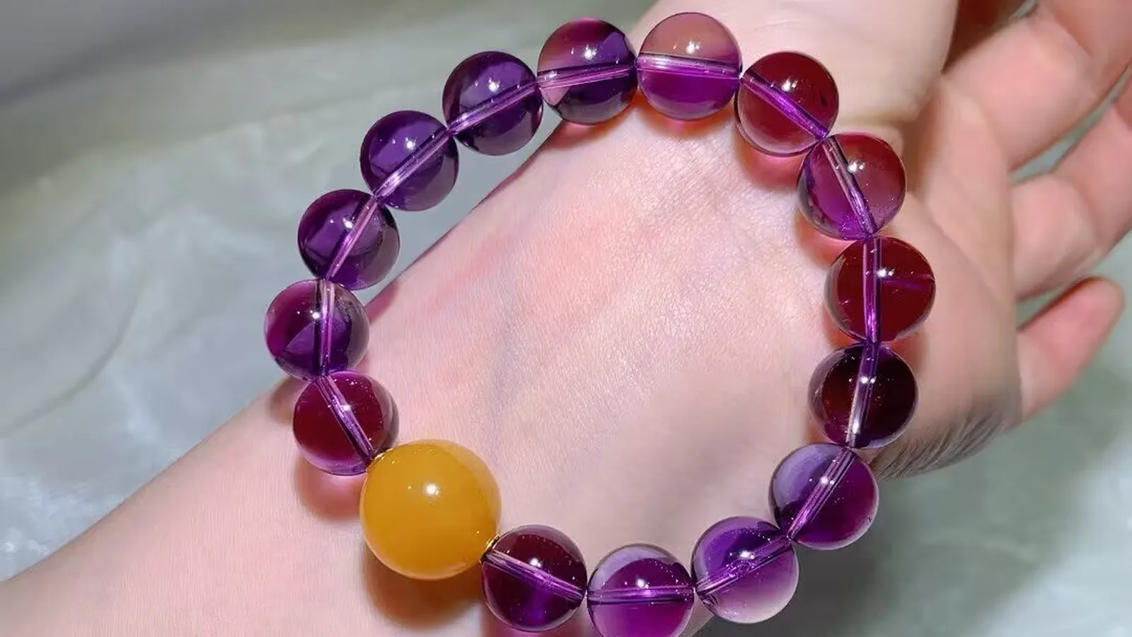 12.3mm amethyst bracelet on a wrist: clear violet to wine-purple beads with one honey-yellow amber bead