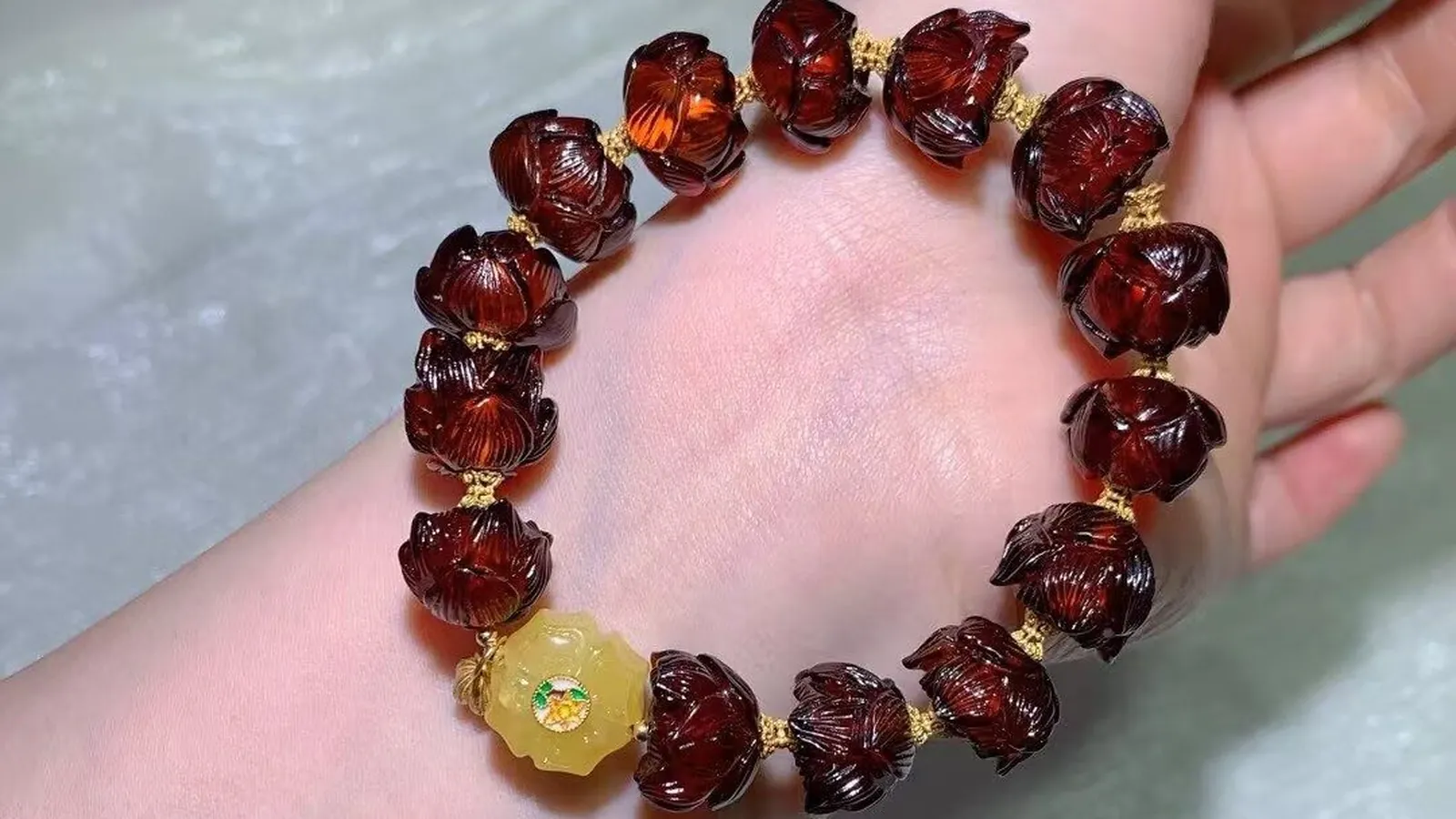 Blood Amber Bracelet with hand-carved cherry-red lotus beads and a honey-yellow amber centerpiece on a hand