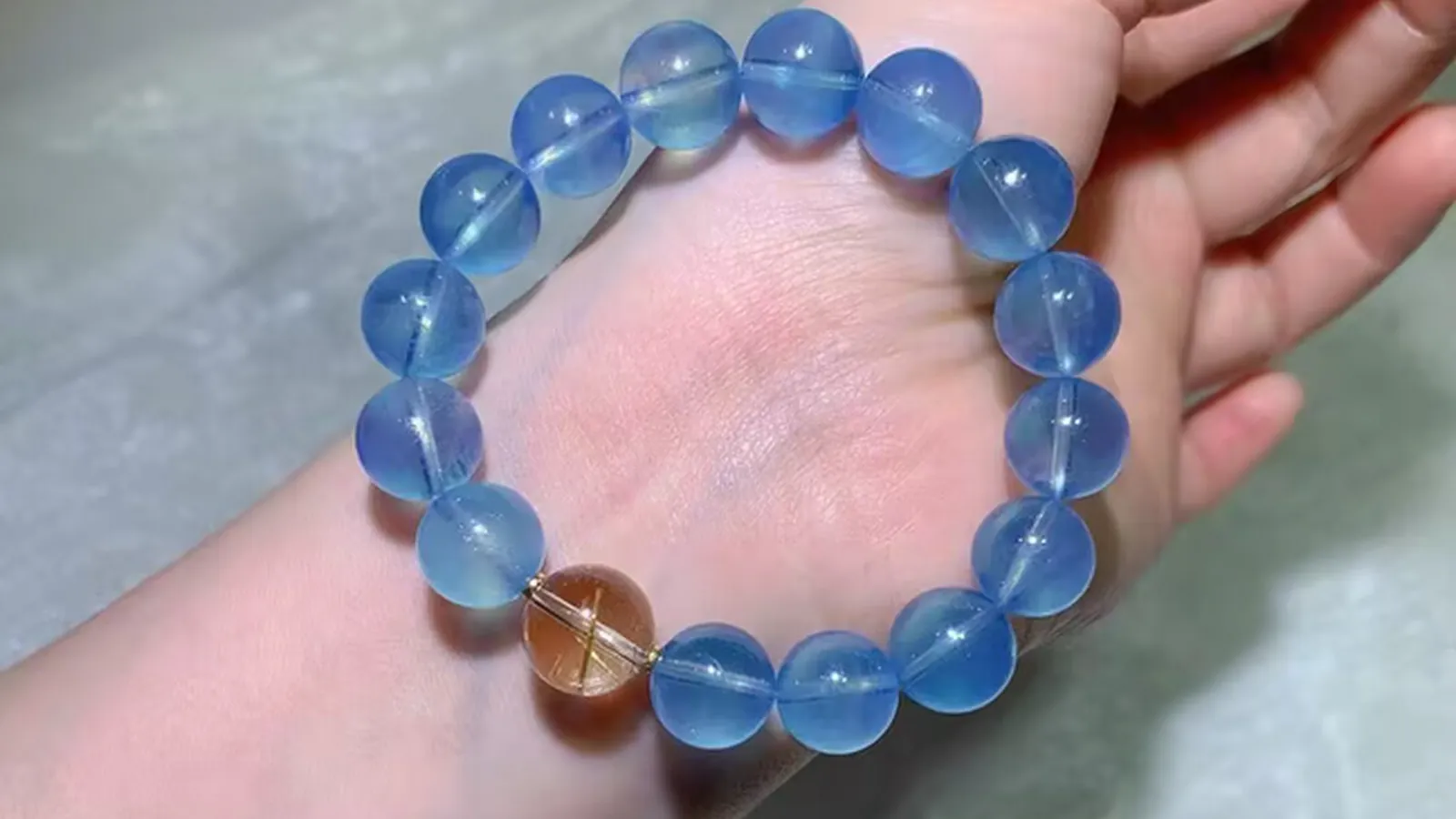 Aquamarine Bracelet 12mm with icy glacier-blue beads and one rutilated quartz accent bead on a hand