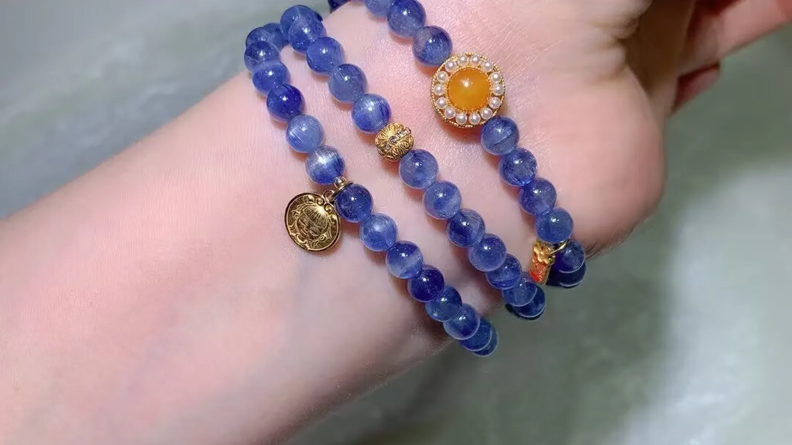 A kyanite multi-wrap bracelet wrapped around the wrist, blue streaked beads with a honey-yellow cabochon and a vintage-style disc charm
