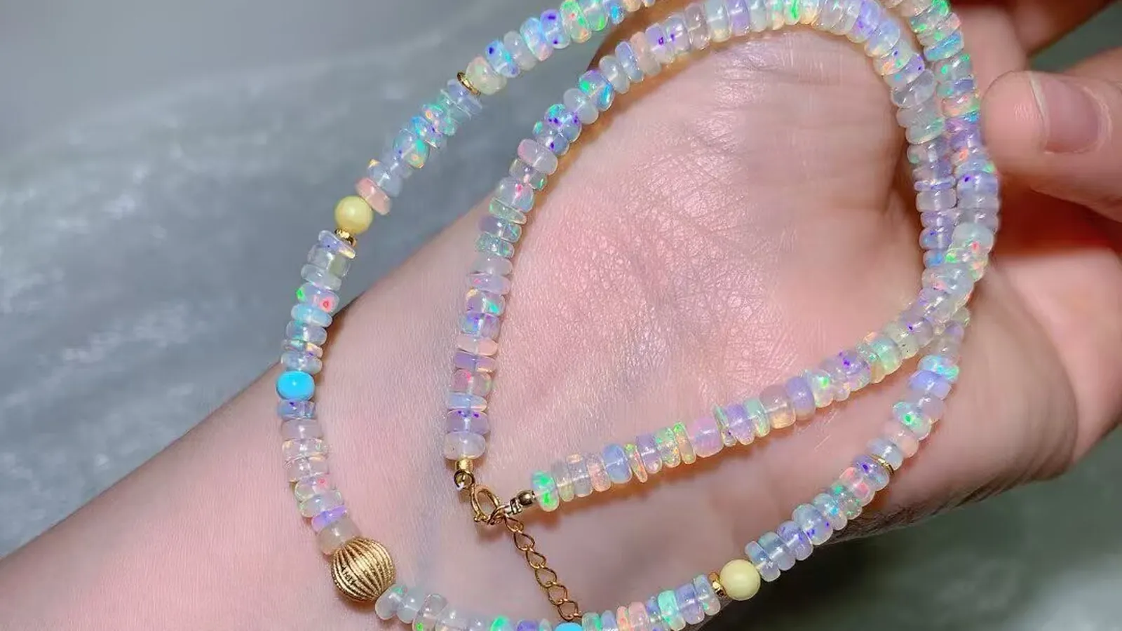 手に取った4.7mmのオパール ビーズネックレス。虹色の遊色がきらめく白いオパールのロンデルに、ヴィンテージ風のリブ模様の丸珠とアジャスターチェーン