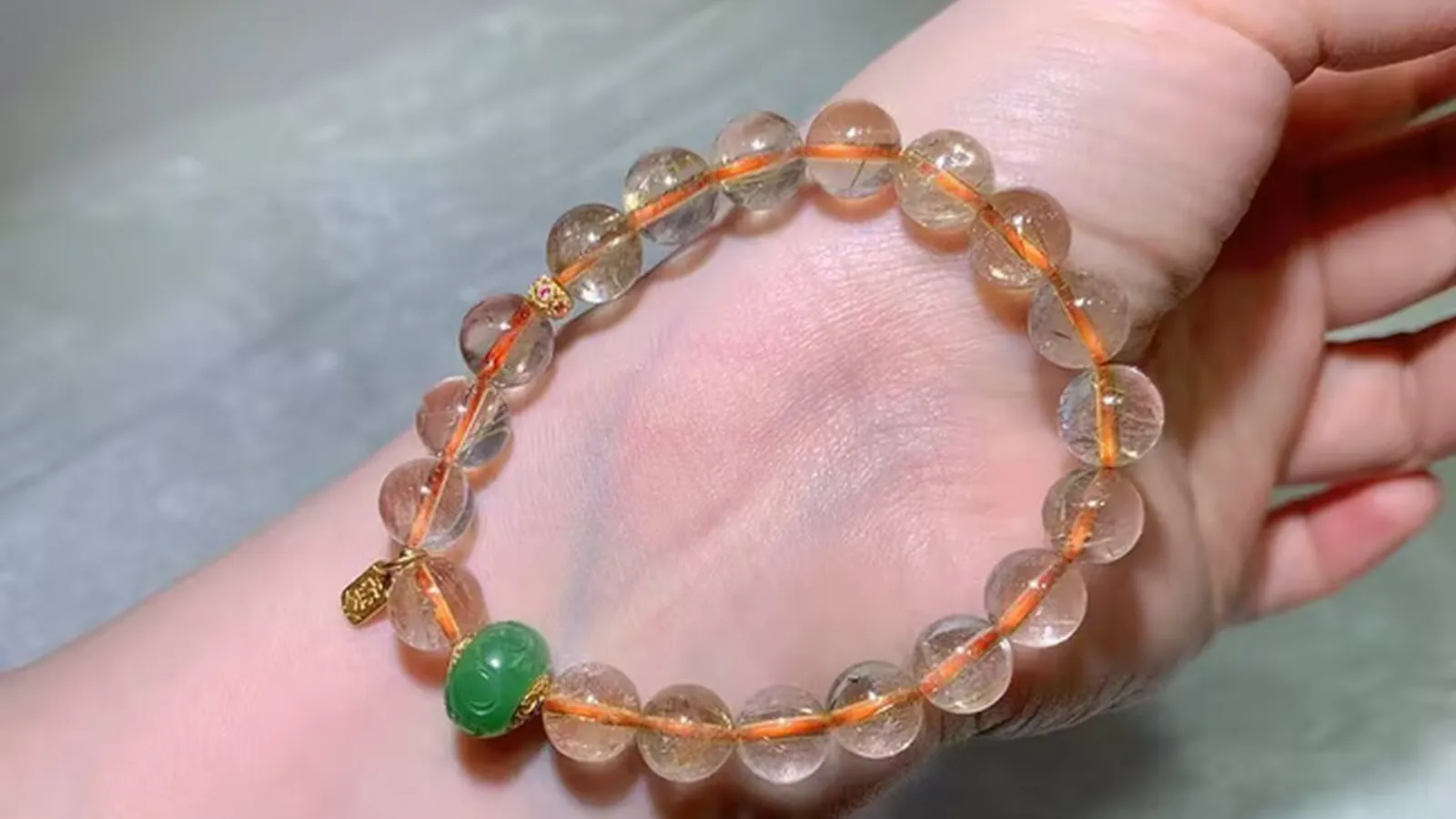手首に着けたタイチンルチルクォーツのブレスレット。細い金色の針が入った透明な珠に、グリーンのアクセント珠とヴィンテージ風アクセント